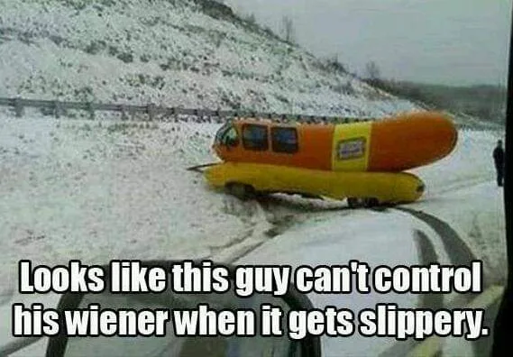 A snow-covered road with a hot dog-shaped vehicle, resembling a hot dog with mustard, stuck sideways on the snowy terrain…