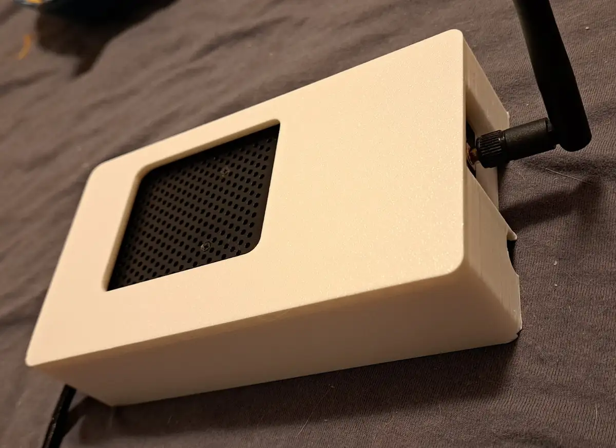 A white, rectangular, 3D-printed box with a black perforated speaker grille on one side and a black antenna attached to the…