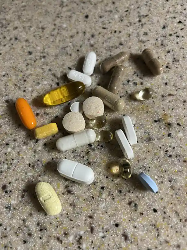 A collection of various pills and capsules, including white tablets, brown capsules, yellow gel caps, and an orange pill…