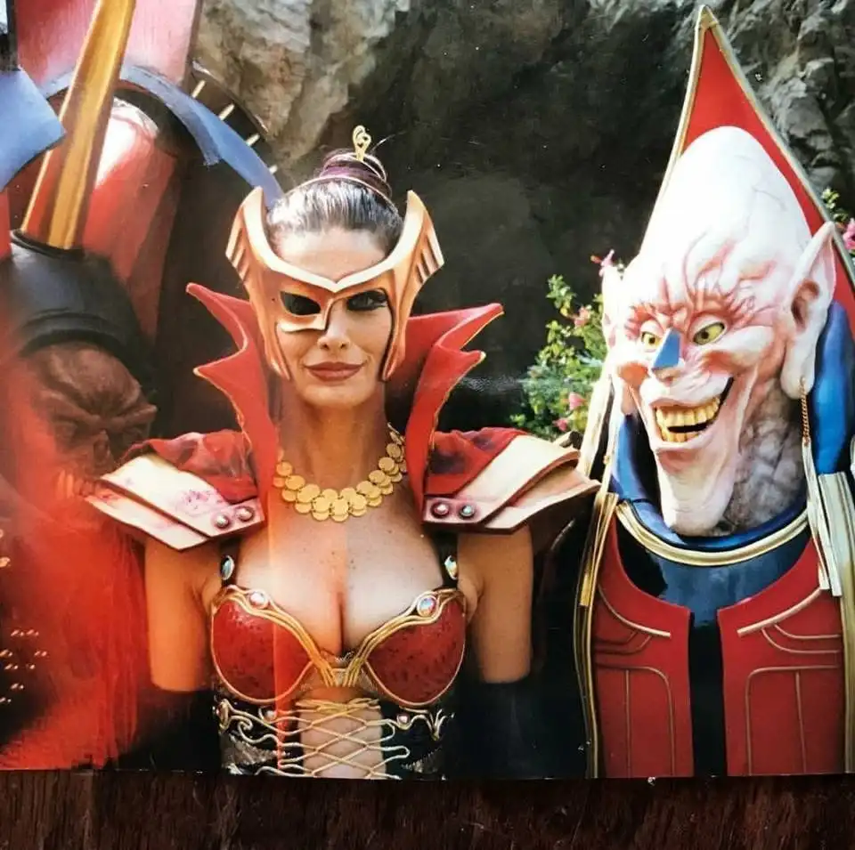A photo shows three costumed characters resembling villains from fantasy or superhero media. The central figure is a woman…