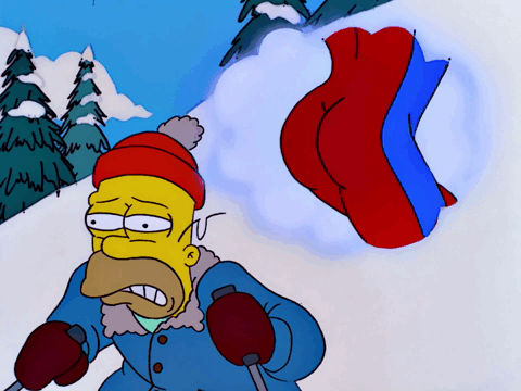 Homer Simpson, wearing a red hat and blue winter coat, stands in a snowy landscape with a grimace, as a large red and blue…
