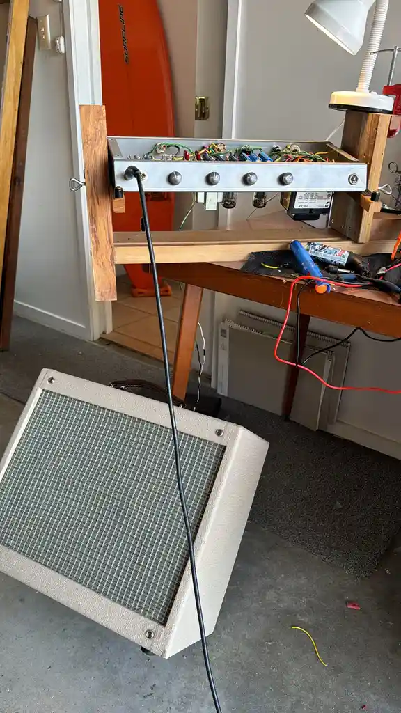A homemade guitar amplifier circuit board is mounted on a wooden workbench, with wires and components exposed. A…