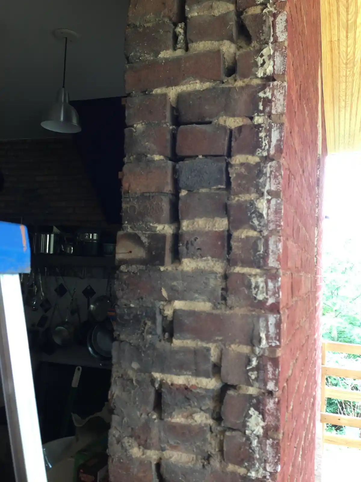 A close-up photo shows a weathered brick pillar with crumbling mortar and darkened bricks, partially obscuring a kitchen…