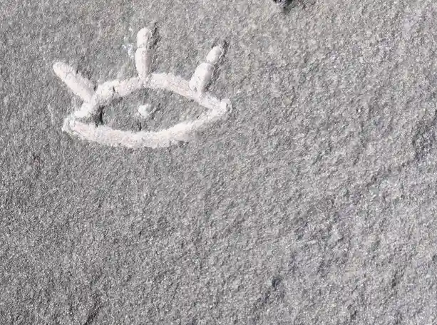 A crude, white chalk drawing of a crown is visible on a gray, textured asphalt surface. The crown has a circular base with…