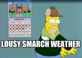 The image shows Homer Simpson wearing a brown hat and green scarf, looking frustrated. Behind him is a calendar for March…