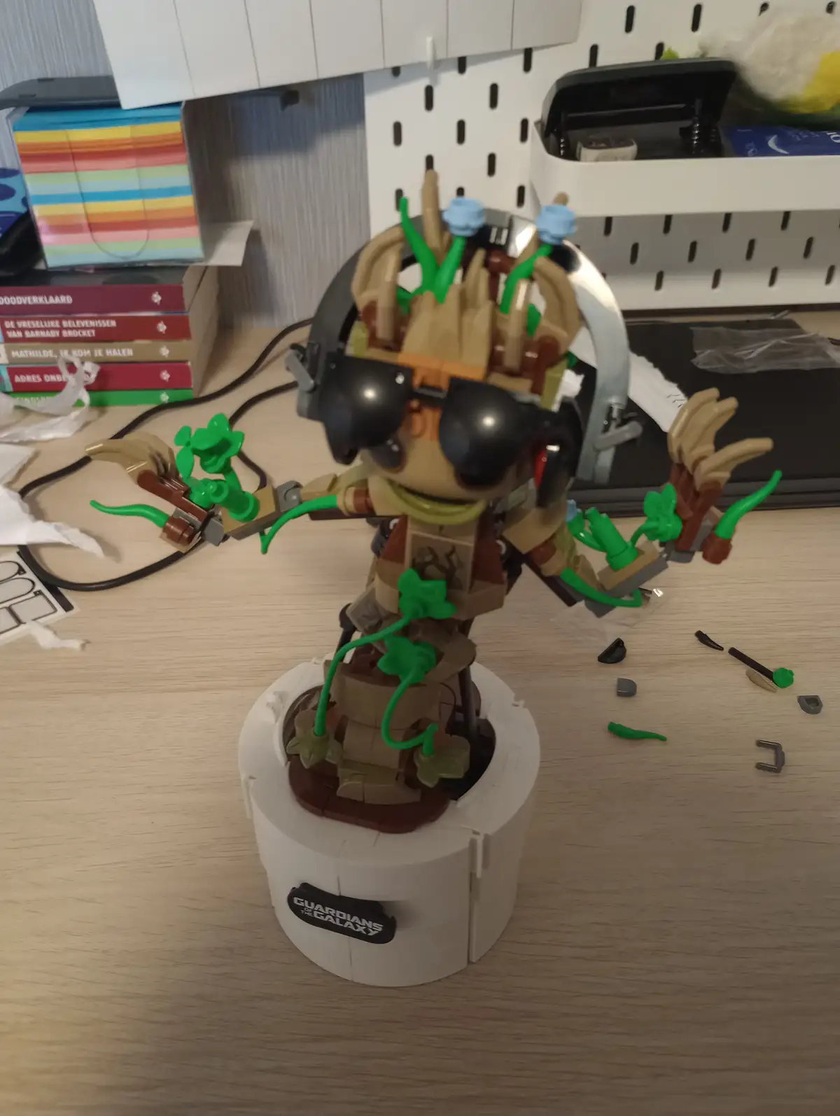 A LEGO Guardians of the Galaxy Groot figure stands on a white base with a 'guardians of the galaxy' logo, wearing black…
