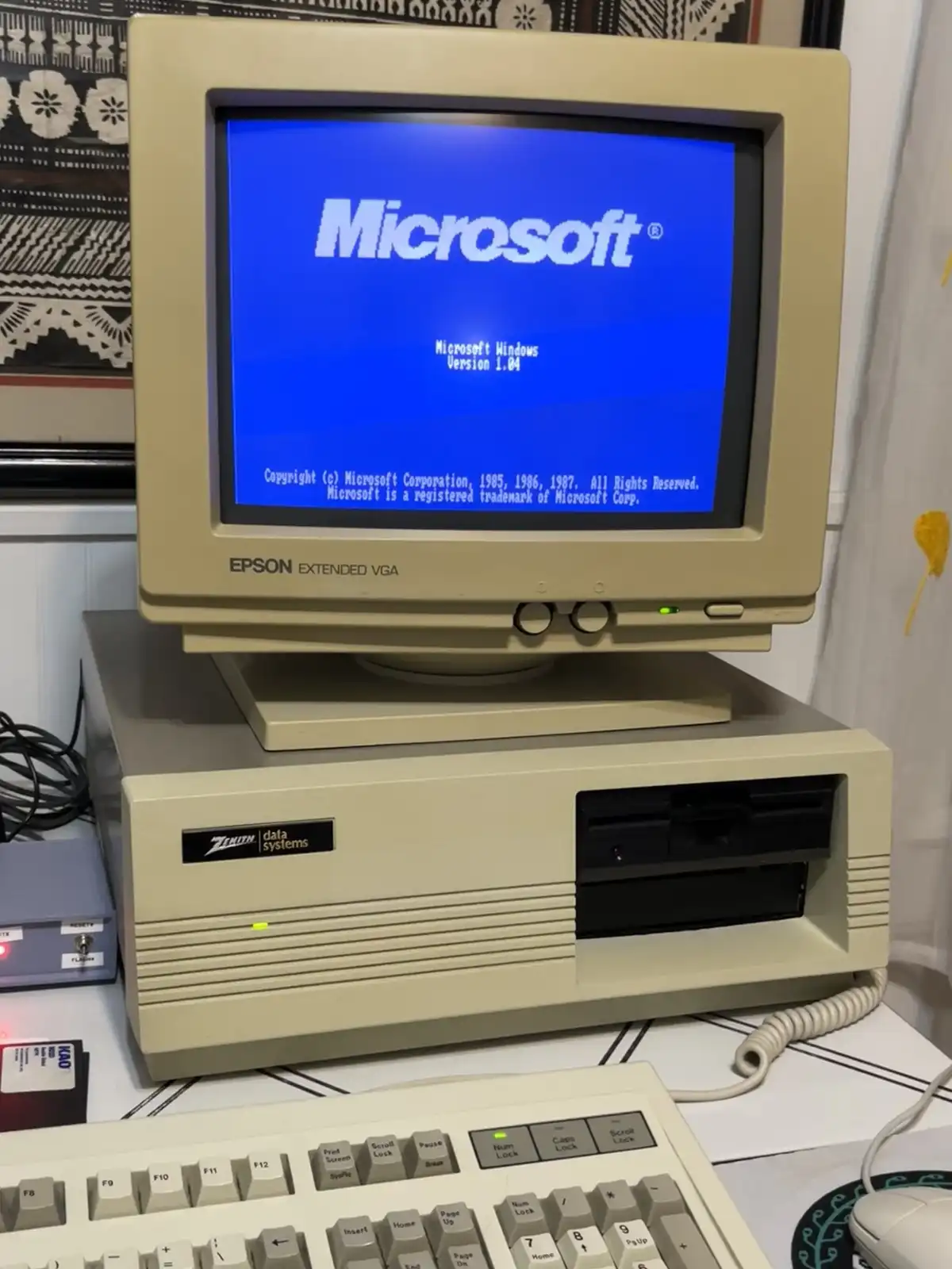An old beige Epson Extended VGA monitor displays the Microsoft Windows Version 1.04 startup screen with copyright text from…