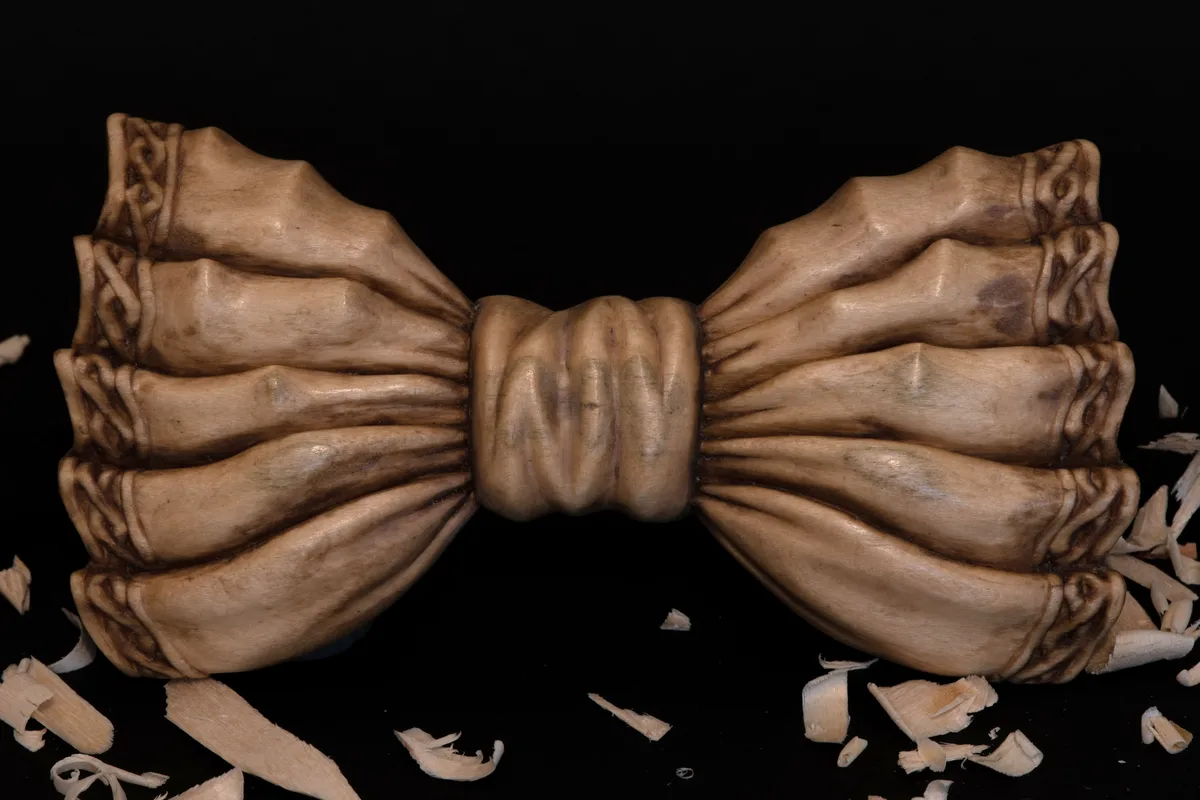 A meticulously carved wooden bowtie, shaped with intricate folds and textures resembling bone, rests on a black surface…