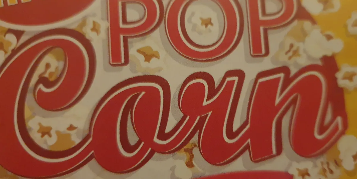 A close-up of a vintage-style popcorn box label with large red text reading 'POP CORN' against a yellow background with…