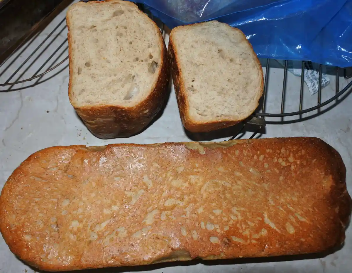 Two slices of bread sit on a wire rack, revealing their porous, light-colored interiors. Below them lies a long…