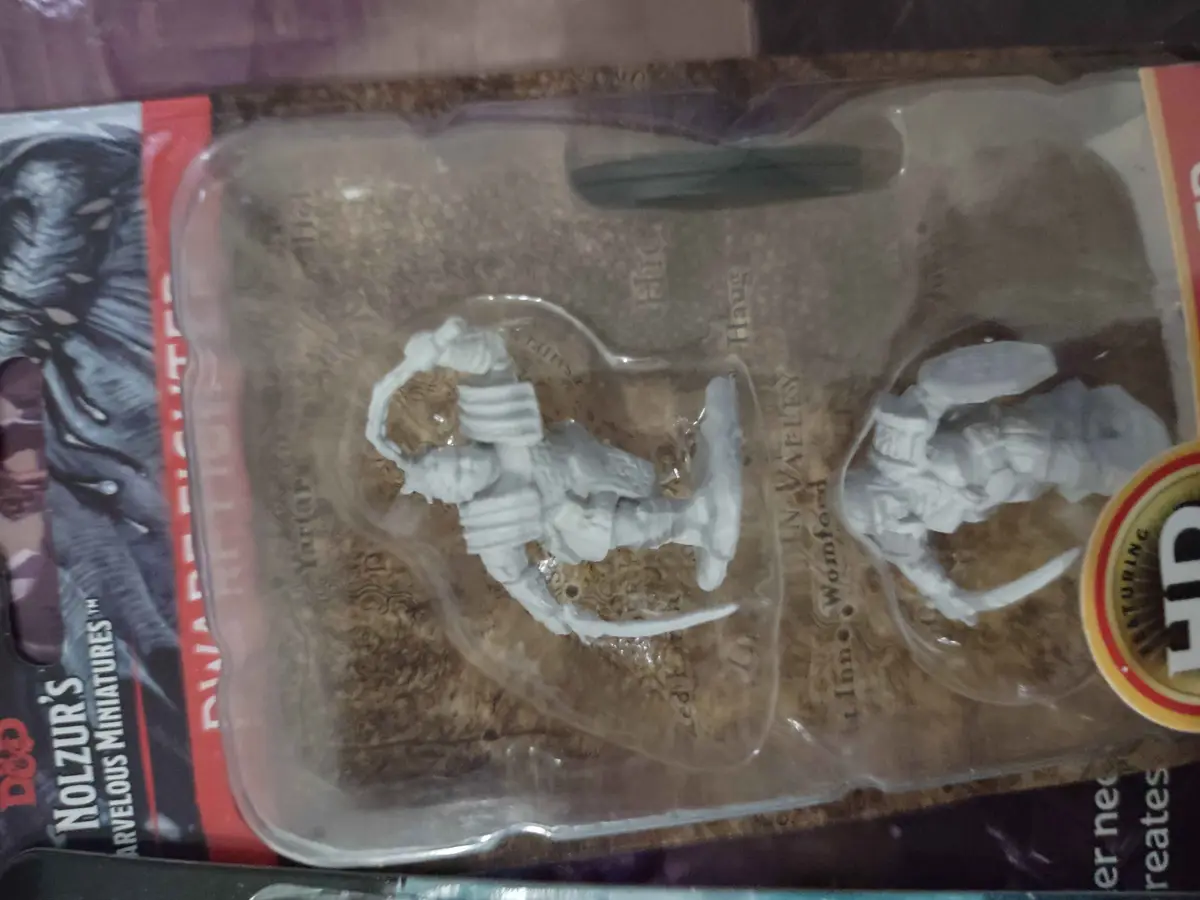 An unopened package of Dungeons & Dragons miniatures shows two unpainted, white plastic figures in their plastic tray. The…