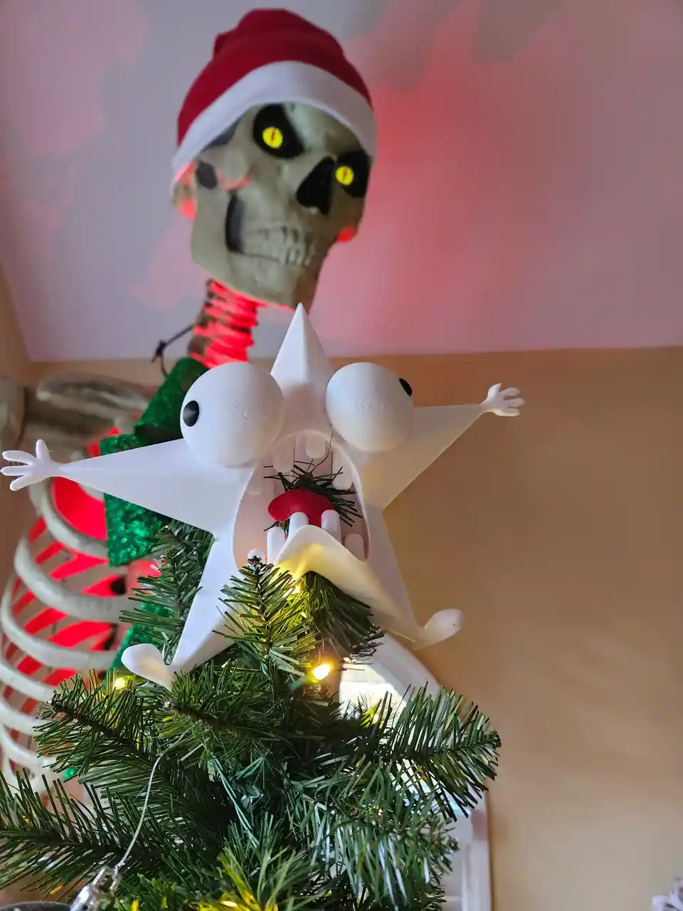 A skeletal figure wearing a red and white Santa hat stands behind a small Christmas tree, which has a white, star-shaped…