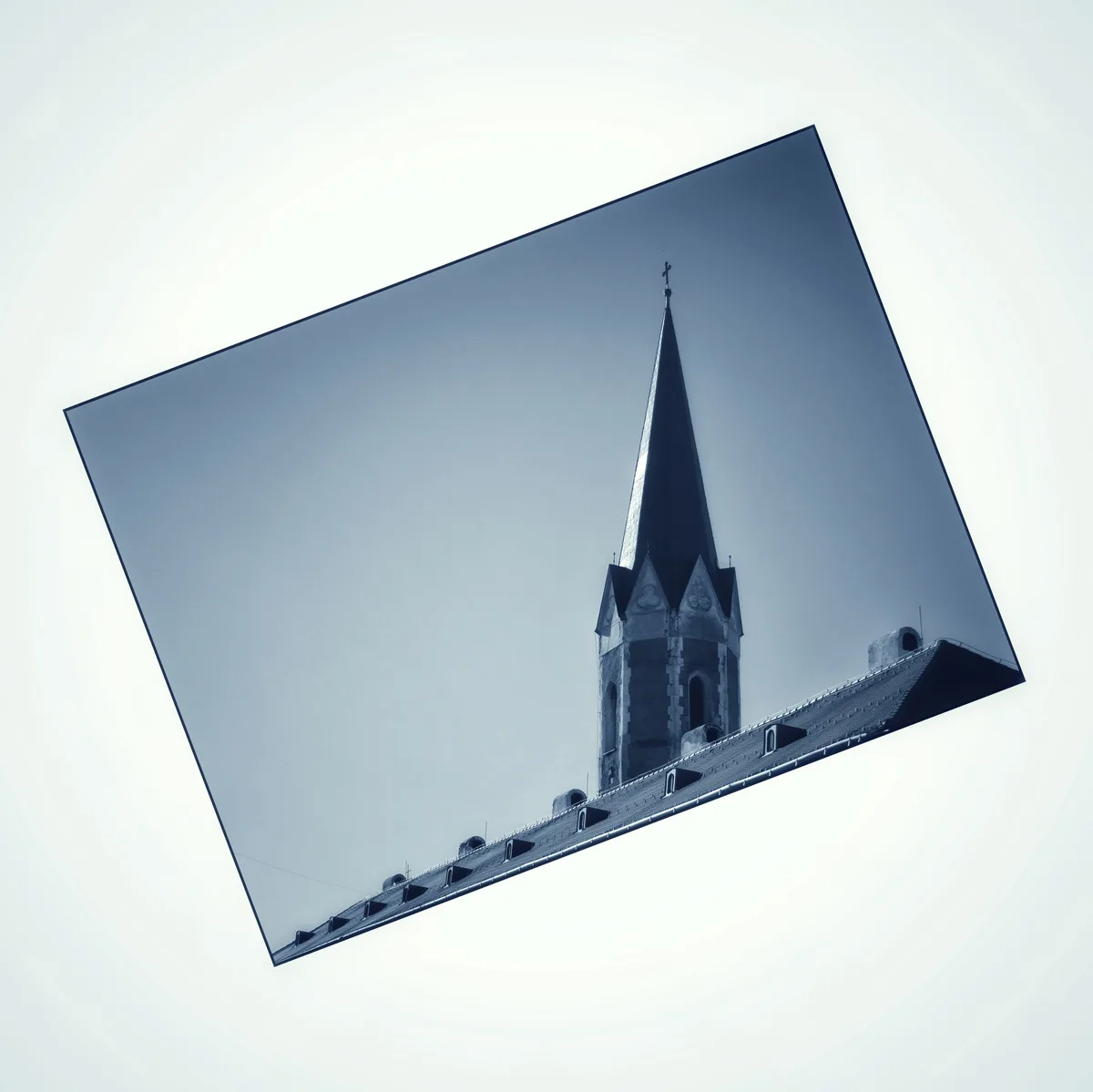 A tilted, sepia-toned photograph of a church steeple with a cross on top, set against a pale sky, framed within a rotated…