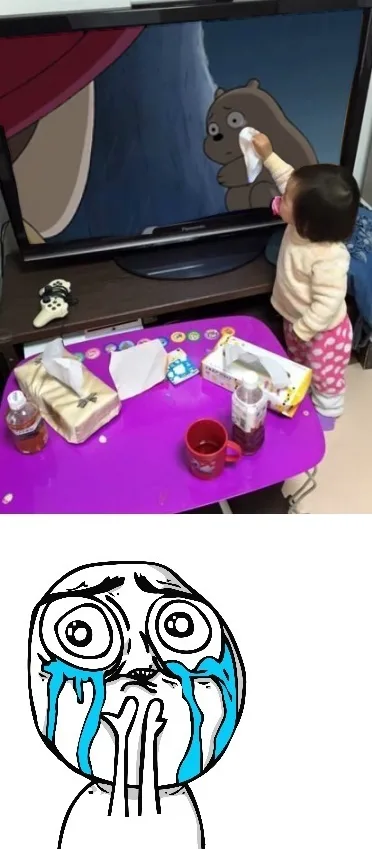 A young child stands in front of a TV, holding a tissue to wipe tears from a cartoon bear on screen. The child is wearing a…