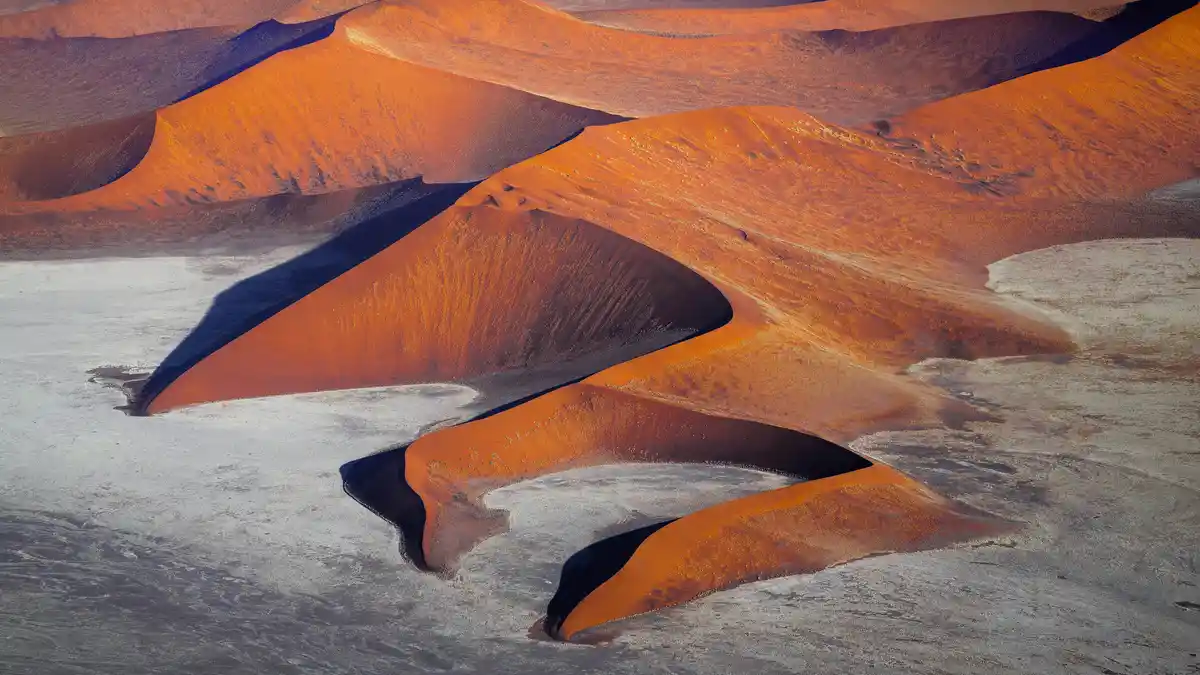 In Namibia's Namib-Naukluft National Park, towering sand dunes age to vibrant red hues due to iron oxide. These ancient…