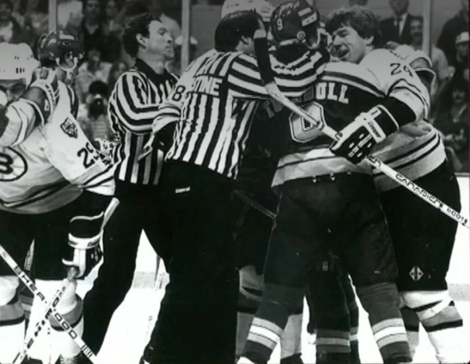 A black-and-white photo captures a chaotic moment in a hockey game where players in striped jerseys are huddled together…