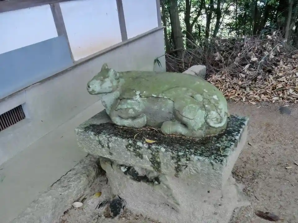 A weathered, moss-covered stone statue of a reclining animal, likely a dog or boar, sits atop a granite pedestal outdoors…