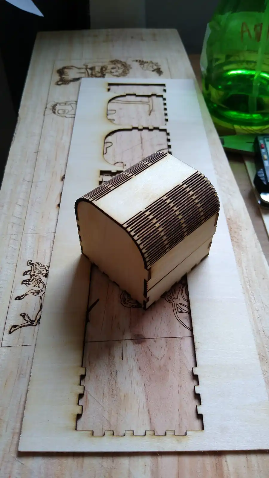 A small, laser-cut wooden chest with a curved top sits on a larger wooden board that has puzzle-piece edges and engraved…