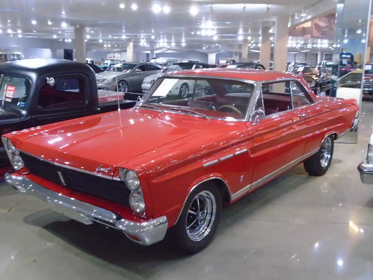 A shiny red 1960s American car, likely a Chrysler Newport or similar model, is displayed in a well-lit indoor car showroom…
