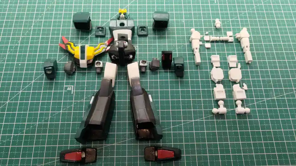 A green cutting mat displays a partially assembled plastic robot model with its parts scattered around it, including a…