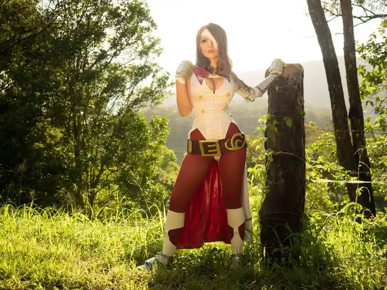 A person in a detailed cosplay of the video game character Ashe from Team Fortress 2, standing outdoors in a grassy, wooded…