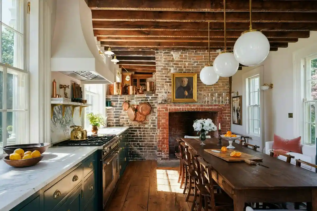 a high-end kitchen with exposed wooden beams, a brick fireplace, copper pots hanging on the wall, and a long wooden dining…