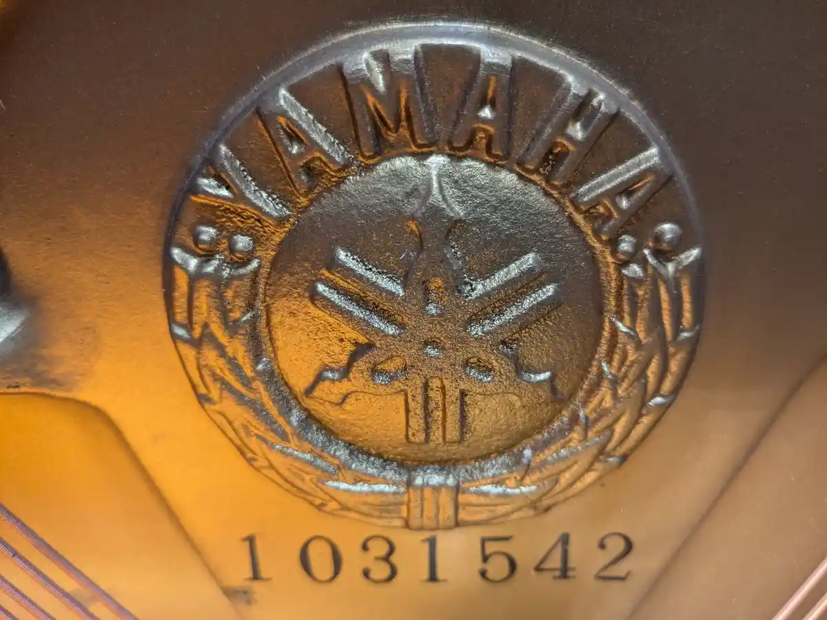 A close-up of a Yamaha piano's metal logo plaque, showing the embossed 'YAMAHA' text around a central treble clef symbol…