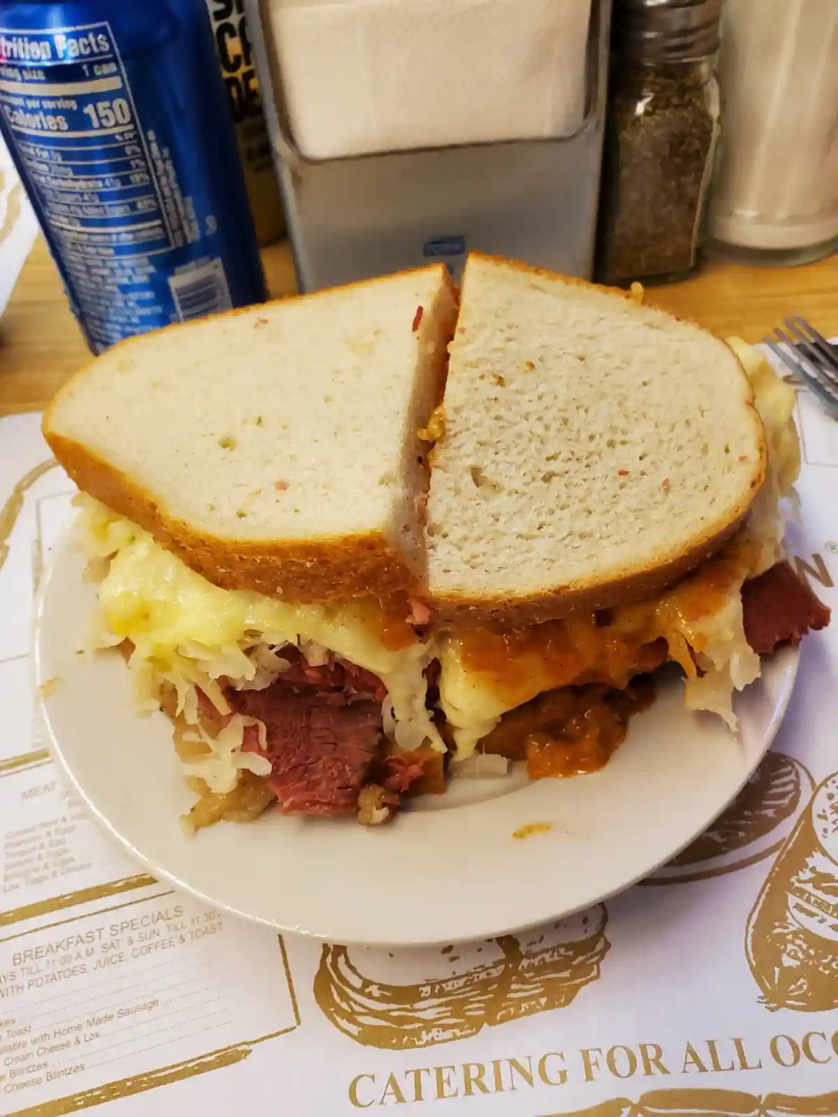 A close-up photo of a large, overstuffed sandwich cut in half, revealing layers of corned beef, melted cheese, and…
