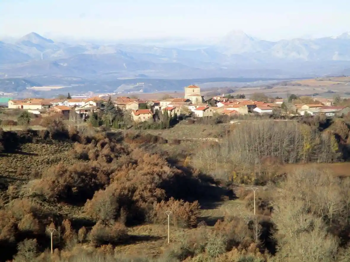 A scenic landscape photo of a small village with red-tiled roofs nestled in autumnal hills, with distant mountains under a…