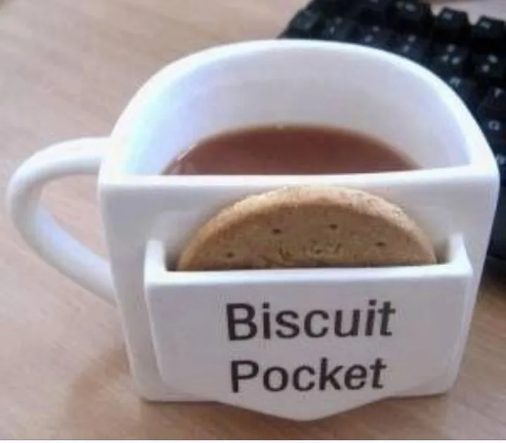 A white ceramic mug with a built-in compartment labeled 'Biscuit Pocket' holds a round biscuit while the main body contains…