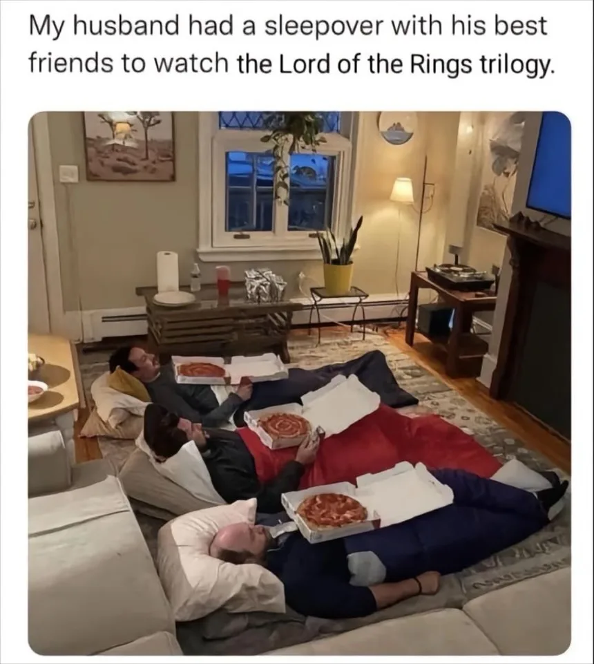 Three men are lying on the floor in a living room, each with a pizza box open on their chest, appearing to be asleep or very…