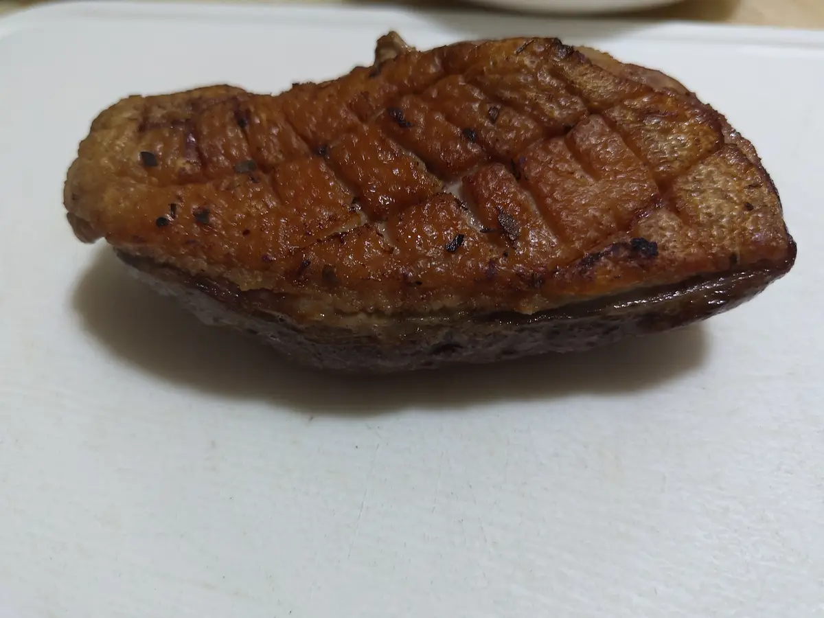 A close-up photo shows a single, perfectly seared duck breast with a golden-brown, scored skin resting on a white cutting…