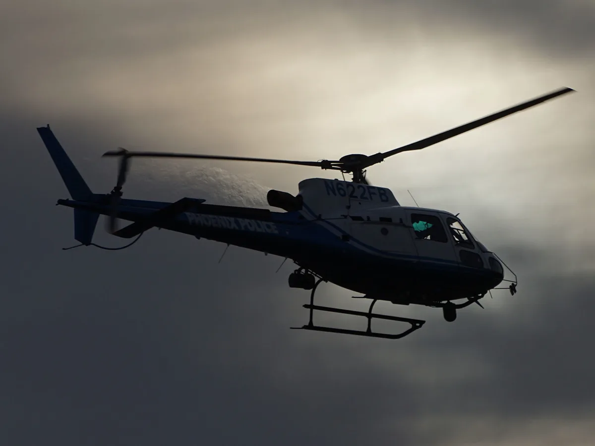 A silhouette of a Phoenix Police helicopter in flight against a cloudy sky, with the text 'phoenix police' overlaid on the…