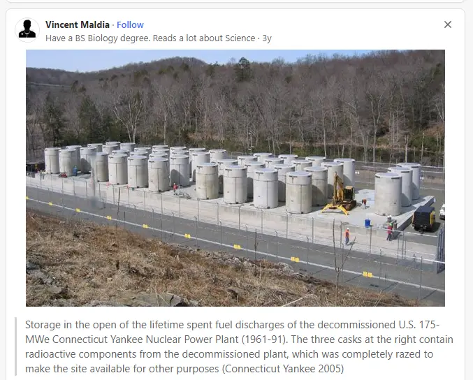 An outdoor photo shows rows of large, cylindrical concrete casks arranged on a paved area behind a fence, with a forested…