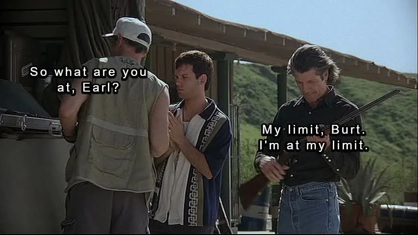 Three men stand outdoors under a covered patio. The man on the left, wearing a white cap and vest, asks 'So what are you at…