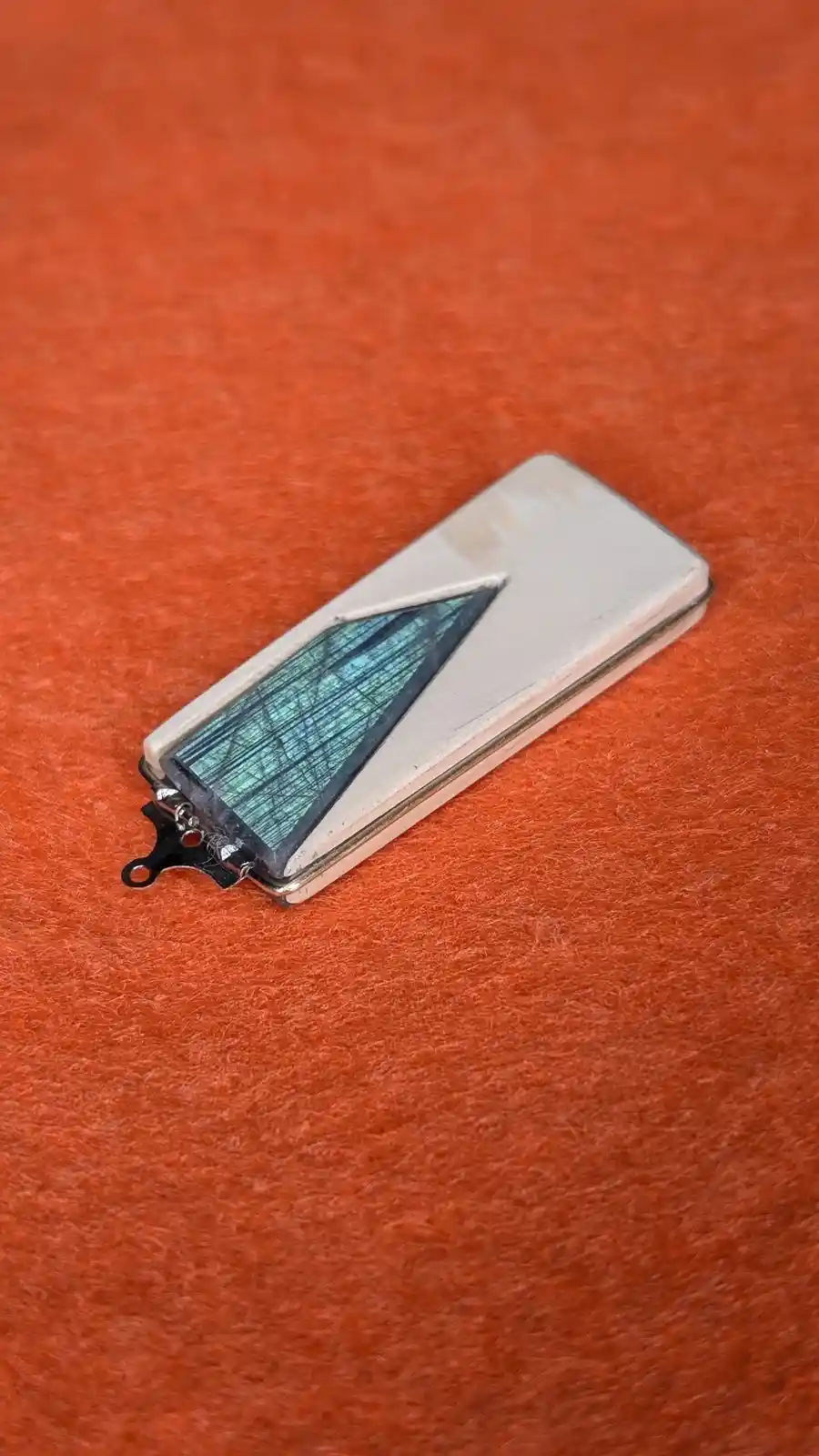 A rectangular pendant with a silver-colored metal casing and a triangular blue-green labradorite stone inset lies on a…