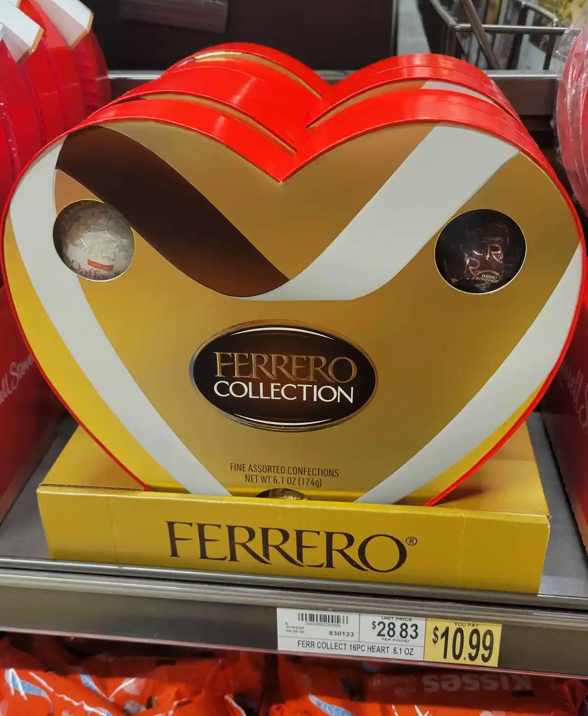 A Ferrero Collection heart-shaped chocolate box sits on a store shelf, priced at $10.99. The box is red and gold with two…