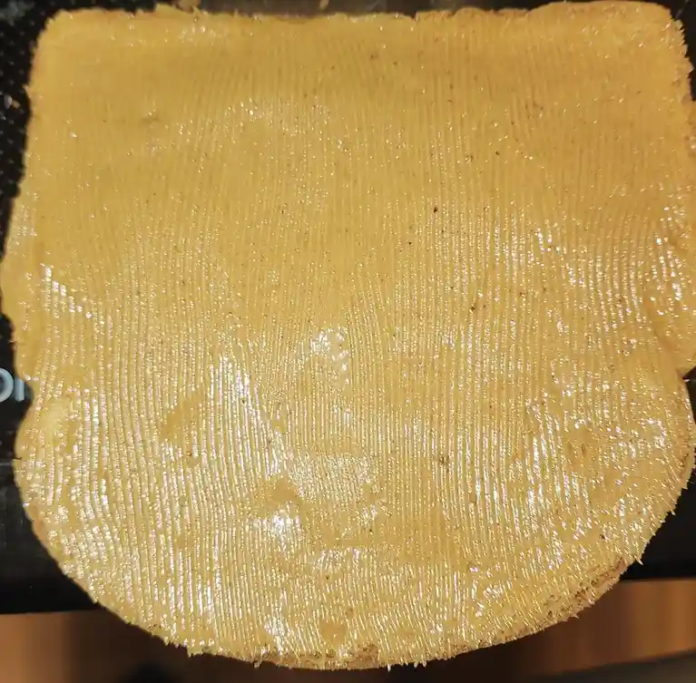 A close-up photo shows a thin, golden-yellow crepe with distinct vertical ridges from a spreader, resting on a dark…