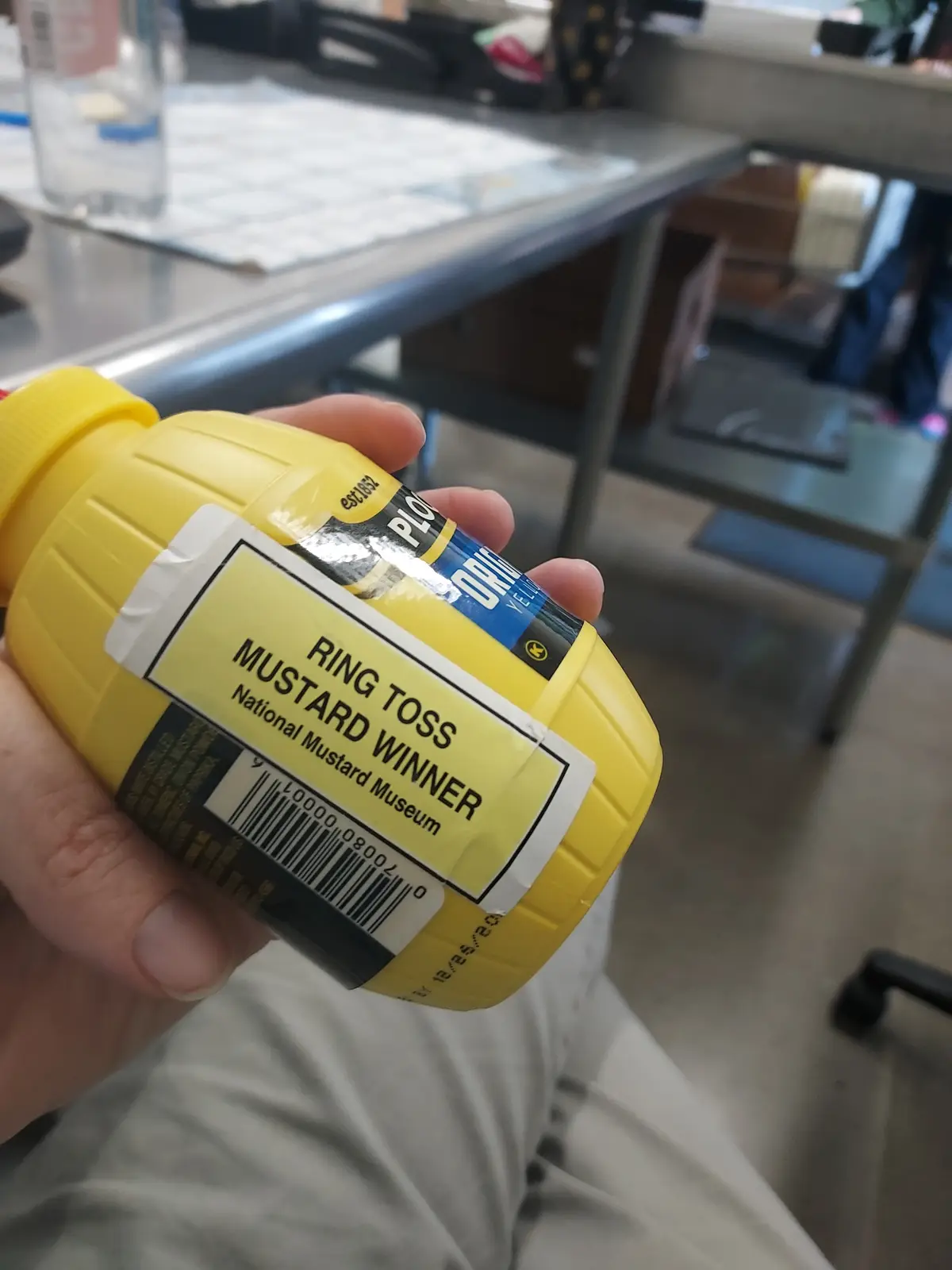 A hand holds a yellow mustard bottle with a custom yellow label that reads 'RING TOSS MUSTARD WINNER National Mustard…