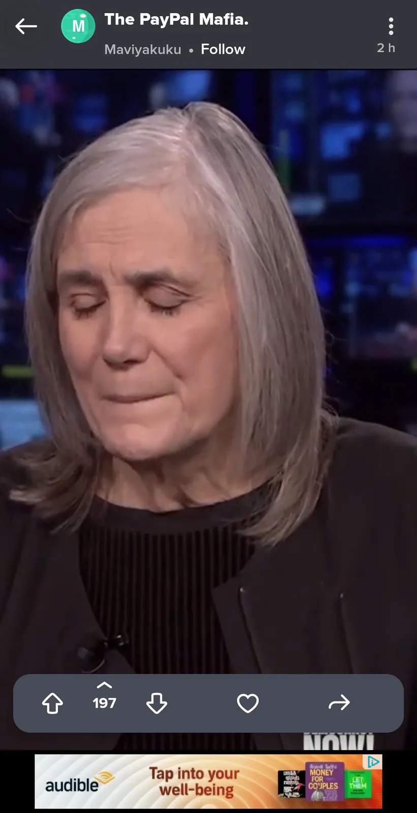 A close-up image of a woman with gray hair, eyes closed, and a somber expression, appearing on a news or talk show set. The…