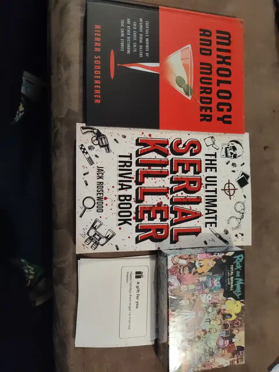 Three items are stacked on a carpeted floor: a book titled 'Mixology and Murder' by Kierra Sonderker, a book titled 'The…