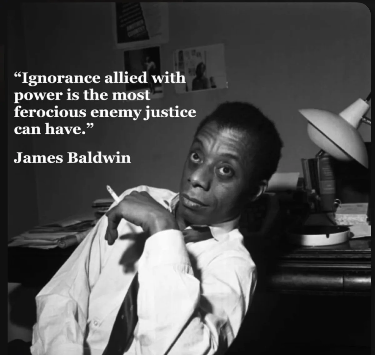 A black and white photo of James Baldwin looking directly at the camera with a serious expression, holding a cigarette. He…