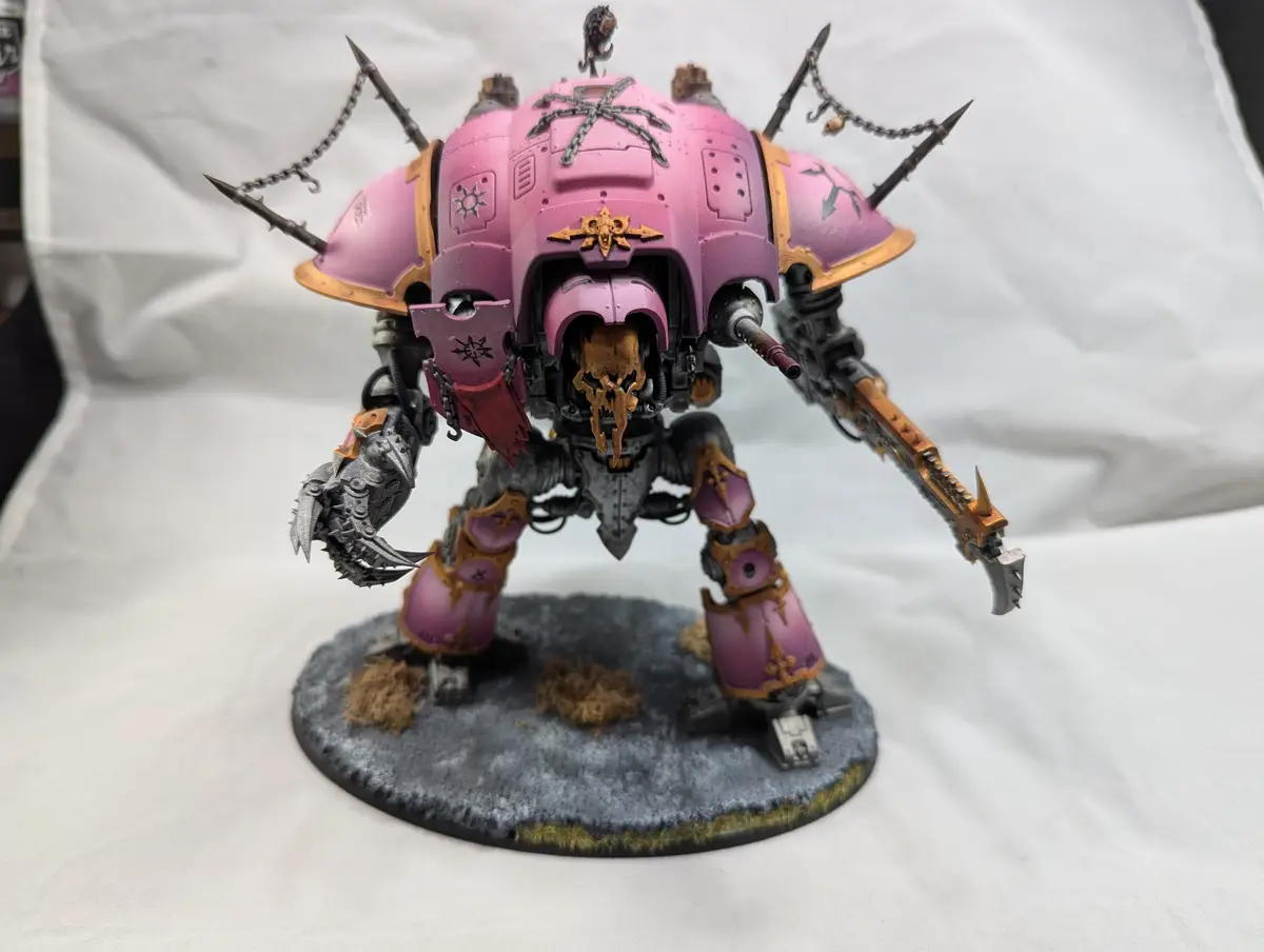 A heavily armored, pink-painted war machine model with spikes, chains, and a skull-like face, standing on a gray base with…