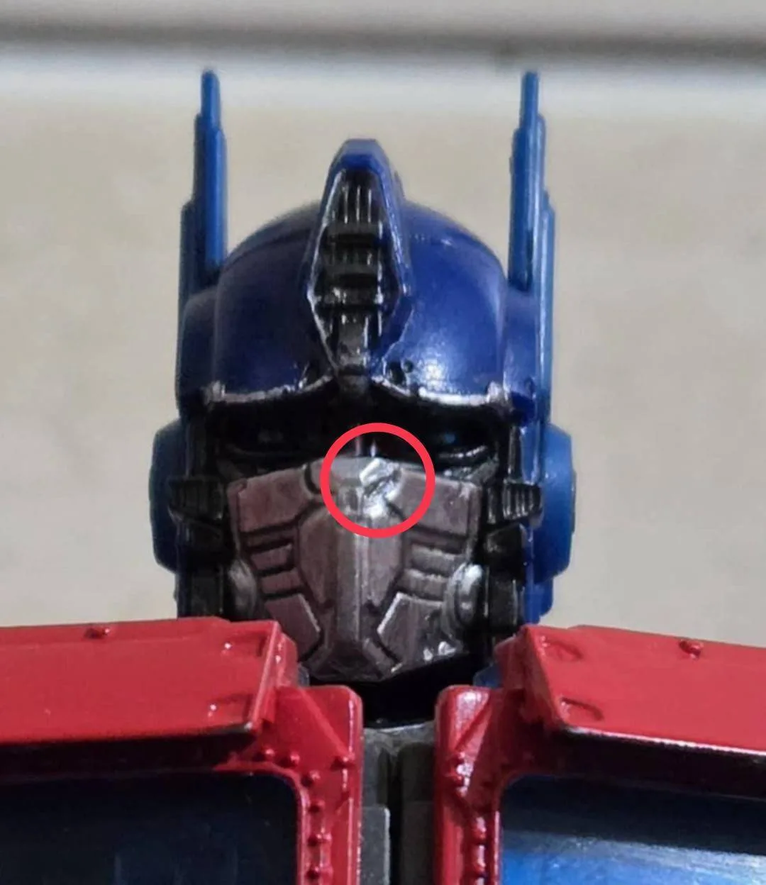 A close-up of an Optimus Prime toy figure highlights a small, shiny, triangular plastic fragment embedded in the center of…