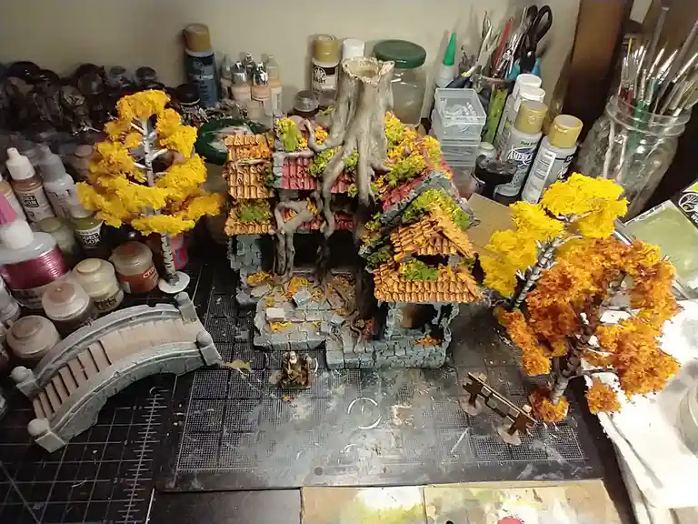 A detailed miniature diorama of a fantasy house with a large tree growing through its roof, surrounded by autumn-colored…
