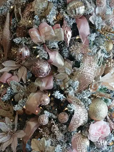 a close-up of an extravagantly decorated christmas tree with flocked branches, pink and gold ribbons, glittery ornaments…
