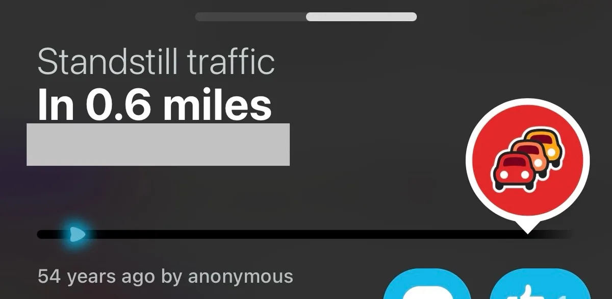 A screenshot of a navigation app interface showing a traffic alert icon with three cartoon cars in a red circle, indicating…