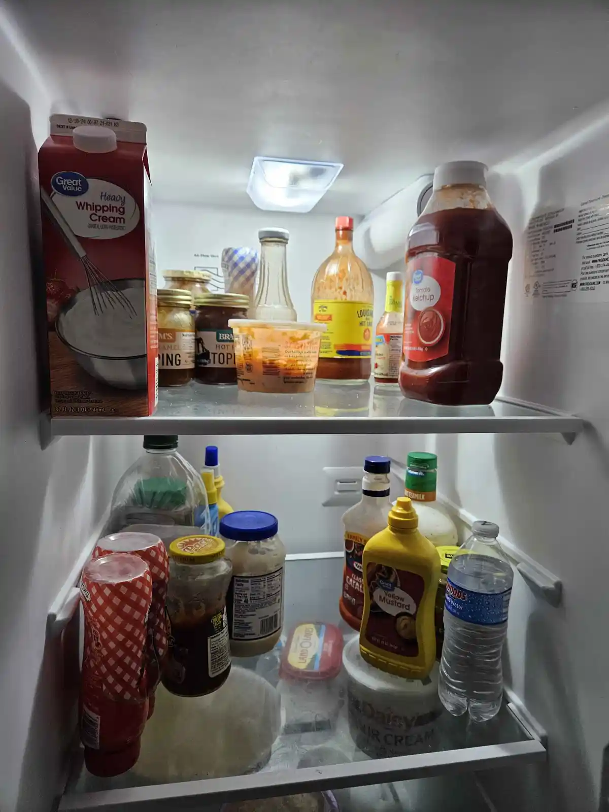 The image shows the interior of a refrigerator with two shelves filled with various condiments and dairy products, including…