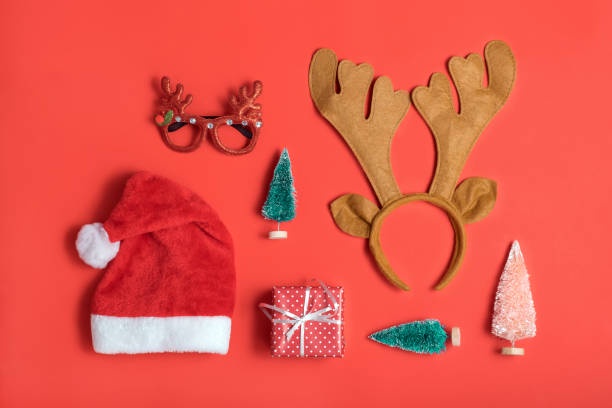 A flat-lay photograph displays various Christmas-themed items including a red Santa hat with white trim, a pair of reindeer…