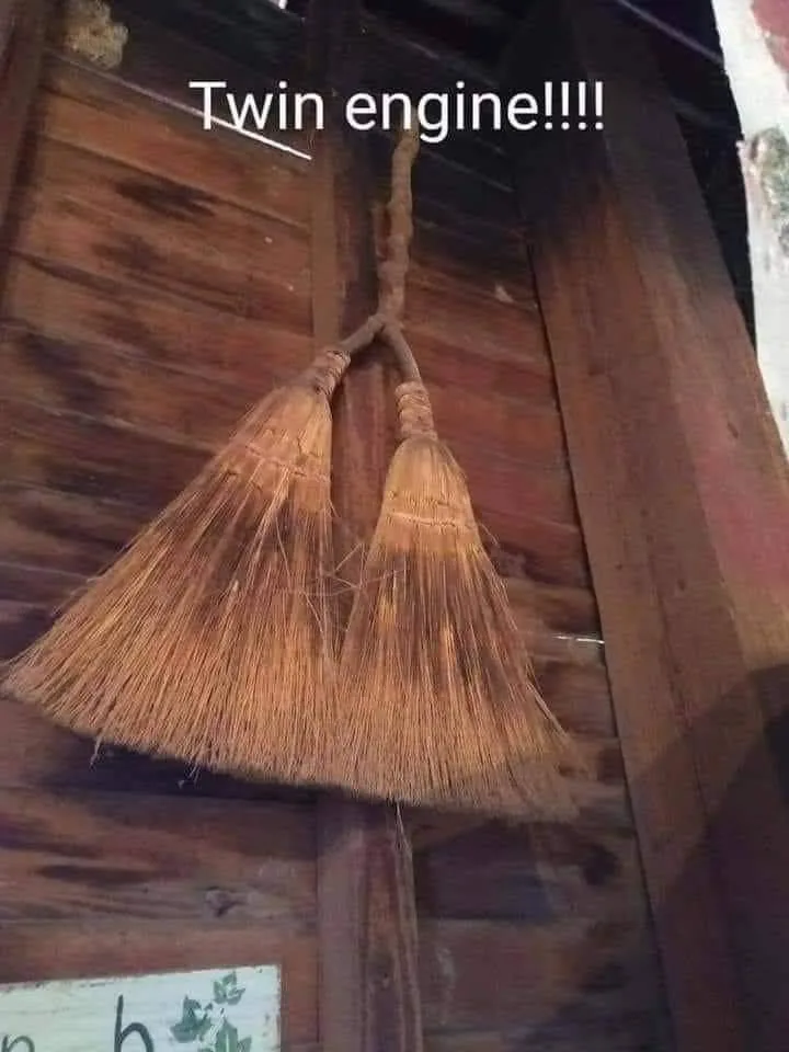 Two brooms with natural bristles are hanging side-by-side from a wooden beam against a rustic wooden wall. The text overlay…